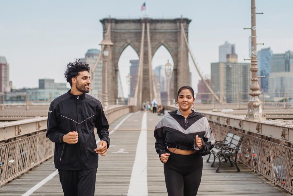 Homens e mulheres praticando corrida na ponte do Brooklyn, símbolo de bem-estar e estilo de vida ativo em uma área urbana de destaque.