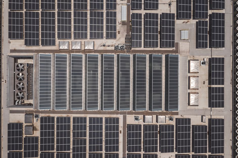 Imagem de telhado de edifício coberto com painéis solares, destacando o uso de energia renovável em construções corporativas.