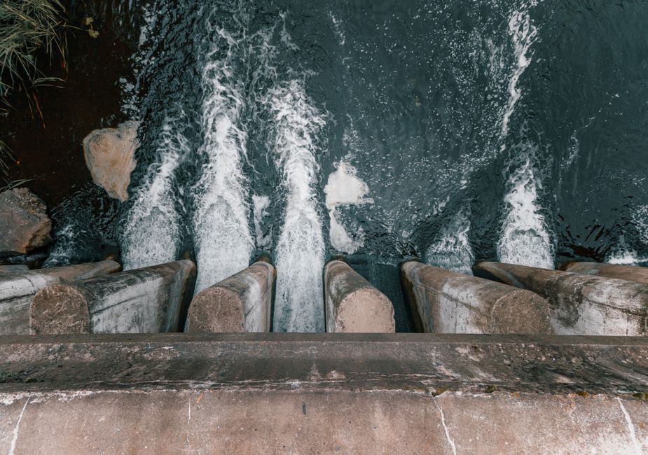 Imagem de uma represa ou barragem com água sendo liberada através de válvulas de controle, simbolizando gestão de recursos hídricos ou produção de energia.
