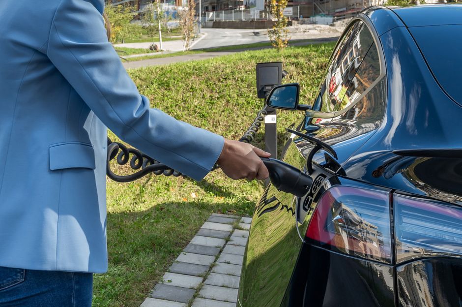 Pessoa carregando um carro elétrico em uma estação de recarga ao ar livre, representando sustentabilidade e mobilidade elétrica.