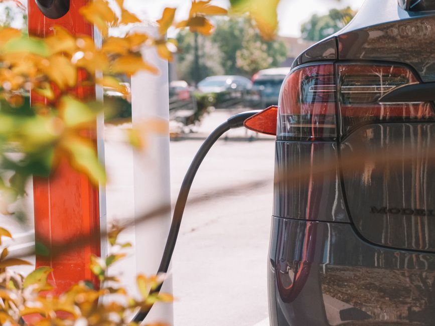 Imagem de um carro elétrico sendo carregado em uma estação de recarga ao ar livre, indicando tendência de sustentabilidade e mobilidade elétrica.