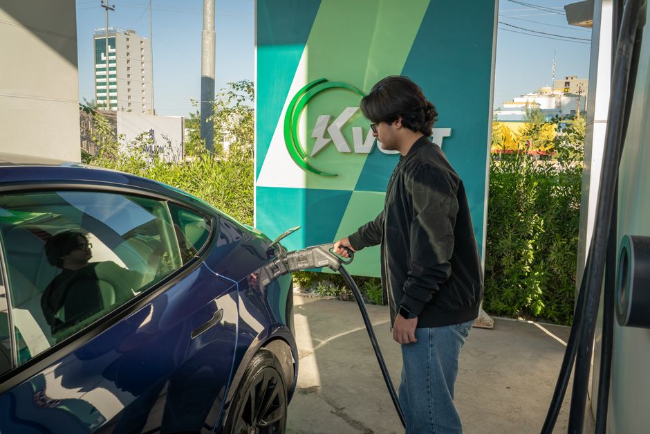 Pessoa carregando um carro elétrico em uma estação de recarga, destacando o tema de mobilidade sustentável e energia limpa.