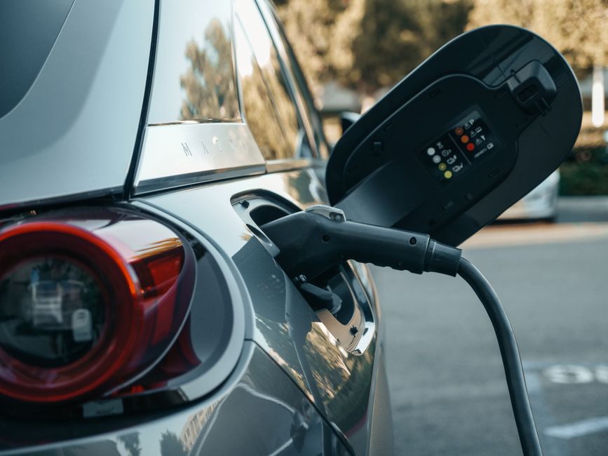 Imagem de um carro elétrico sendo carregado em uma estação de recarga ao ar livre, destacando a tecnologia e sustentabilidade no transporte.