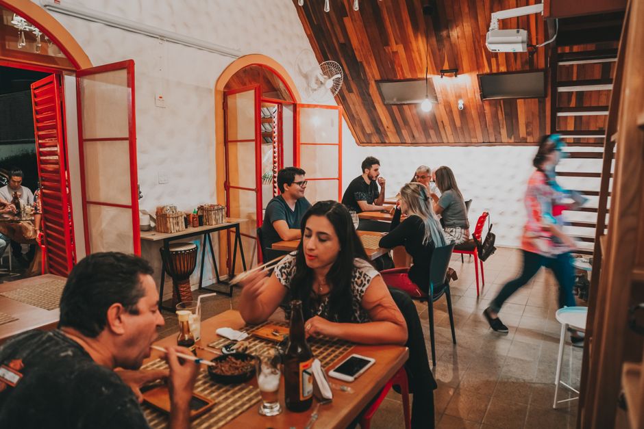 Imagem de um restaurante movimentado com pessoas jantando e conversando em um ambiente com decoração rústica moderna.