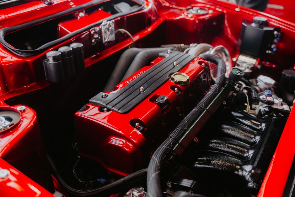 Imagem de um motor de carro de alta performance montado em um compartimento vermelho brilhante, destacando detalhes técnicos e componentes mecânicos.