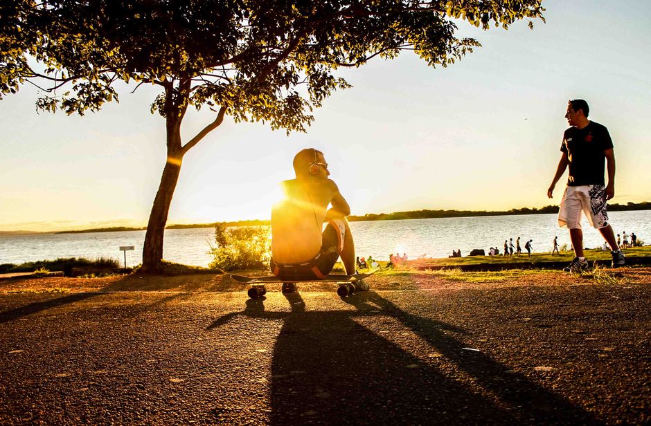 Jovens desfrutando de um pôr do sol ao lado de um lago, com uma atmosfera de liberdade e lazer ao ar livre.