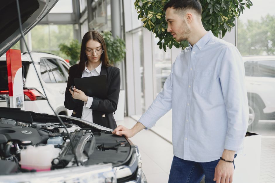 Homem e mulher analisando carro em concessionária, voltado para vendas e avaliação de veículos.