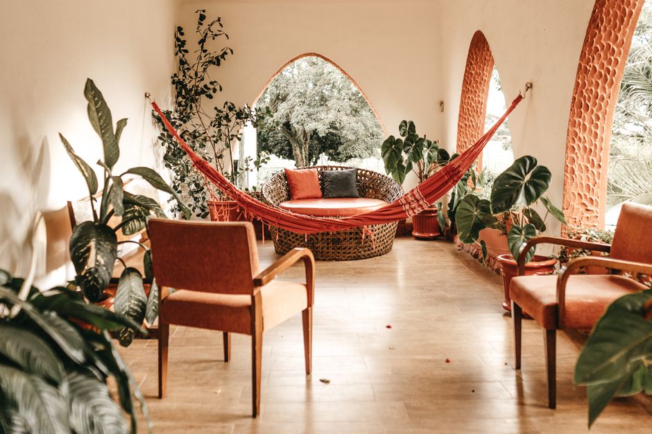 Espaço de convivência tranquilo decorado com plantas, poltronas e uma rede pendurada, ideal para relaxar ou conversar em um ambiente natural e acolhedor.