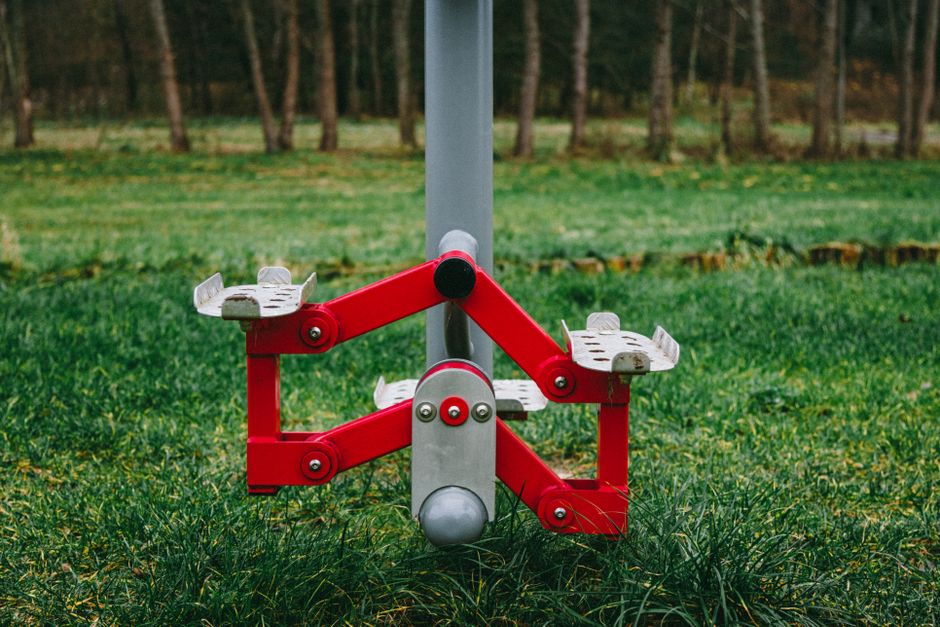 Imagem de um playground ao ar livre com um equipamento de escalada em forma de robô, localizado em um parque com árvores ao fundo.