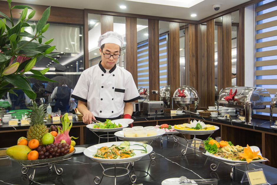 Chef preparando salada em buffet de alimentos, destacando a gastronomia e qualidade na apresentação de refeições em um restaurante sofisticado.