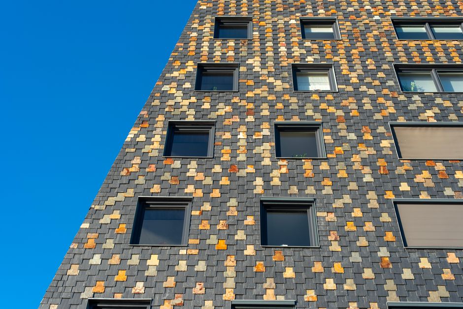 Fachada de um edifício residencial com detalhes em azulejos coloridos e janelas modernas contra um céu azul claro.