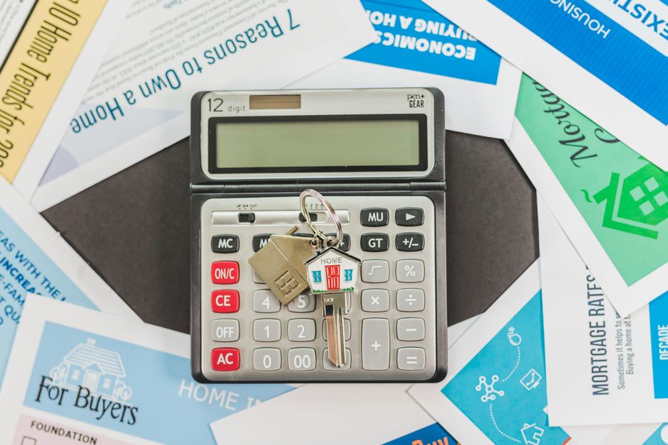 Imagem de uma calculadora com chaves de casa e de carro, sobre documentos relacionados a financiamento imobiliário e de veículos, simbolizando questões financeiras e de crédito.