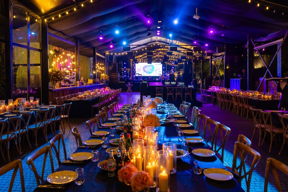 Imagem de uma festa ou evento social decorado com luzes e velas, com música ao vivo ao fundo, em um ambiente elegante e festivo.