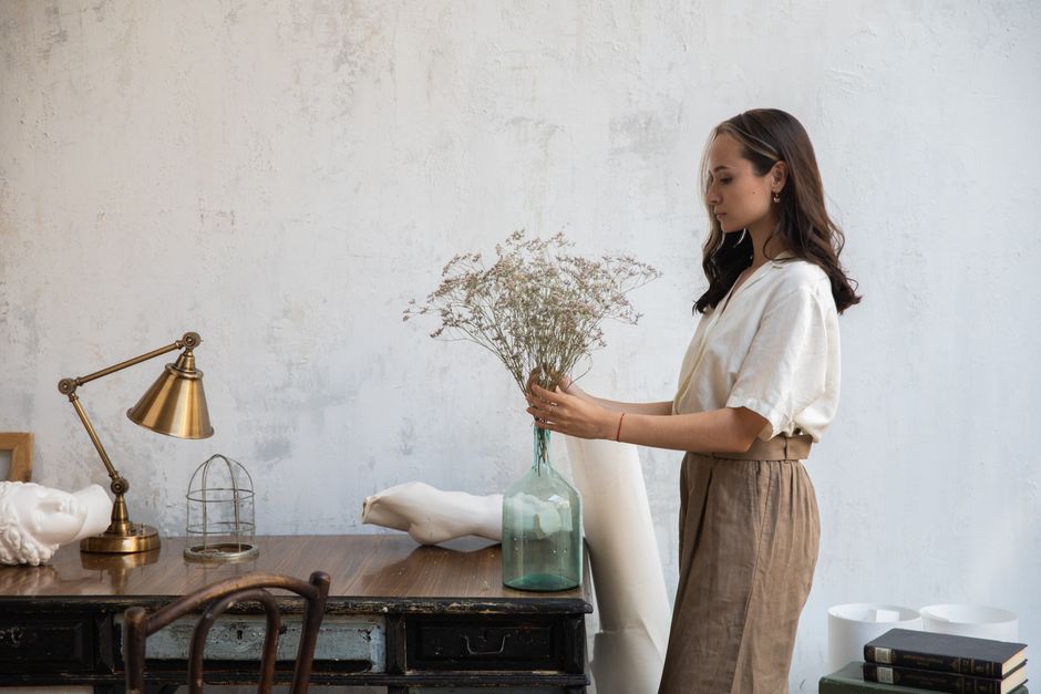 Mulher organizando flores em um ambiente minimalista, refletindo criatividade e atenção aos detalhes para um blog sobre decoração ou bem-estar.