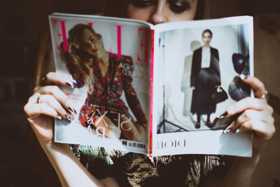 Pessoa lendo uma revista de moda, com foco na descoberta de tendências e estilos atuais.