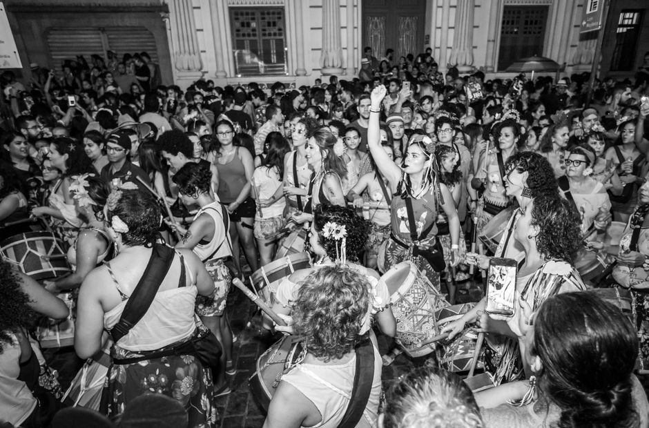 Mulheres participando de uma celebração cultural com dança e música em ambiente público ao ar livre.