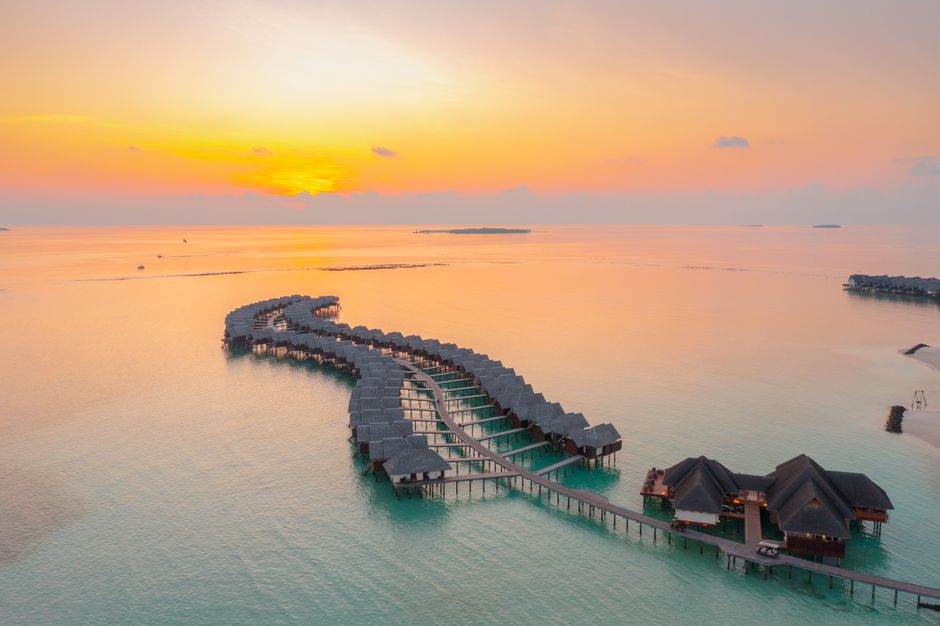 Fotografia de um visual de bangalês de frente para o oceano ao pôr do sol, ideal para ilustrar turismo ou resorts à beira-mar.