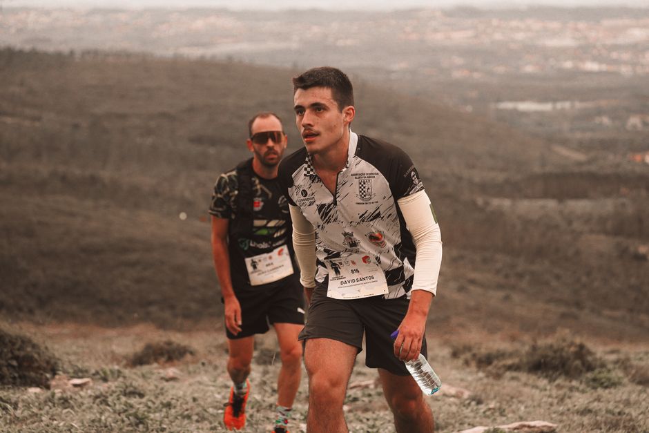 Atletas participando de uma corrida de resistência ao ar livre, em um ambiente árido e com terreno variado, demonstrando esforço e concentração.