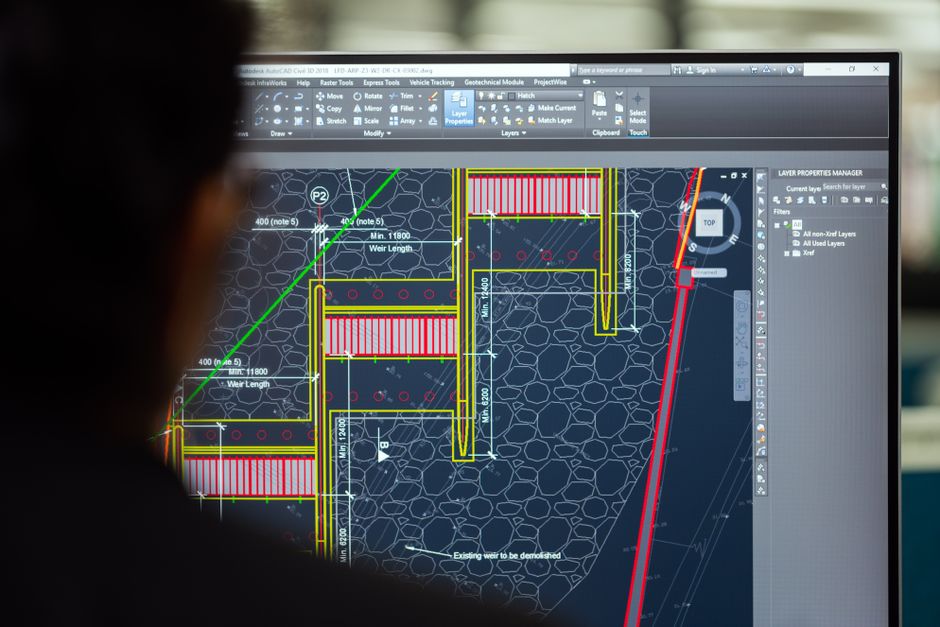 Homem analisando um projeto de engenharia ou arquitetura em software de Design, focado em planejamento e construção de infraestrutura.