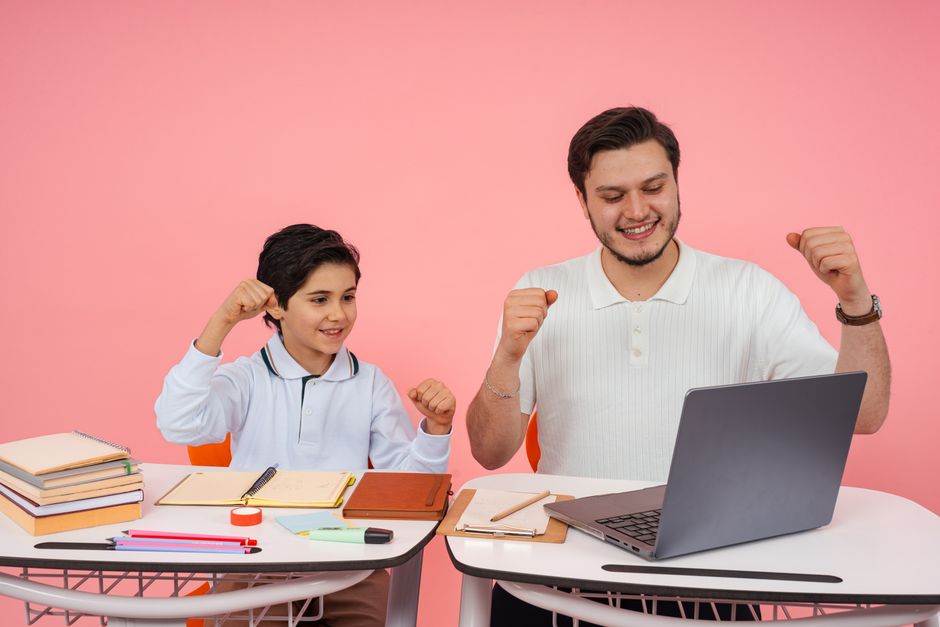 Pai e filho celebrando um momento de conquista estudantil enquanto usam o computador em um ambiente de estudos.