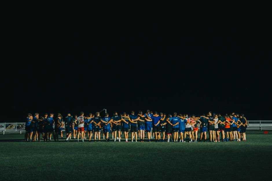Grupo de jogadores de futebol reunidos no campo após uma partida ou treino ao entardecer.
