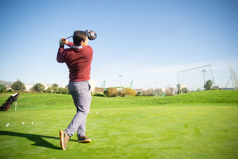 Homem jogando golfe ao ar livre em um campo bem cuidado sob céu claro, representando lazer e esportes ao ar livre.