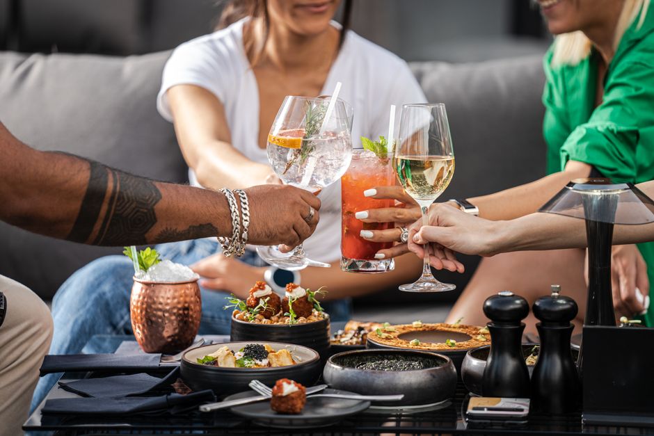Imagem de um grupo de pessoas celebrando com drinks e comida em um ambiente social, promovendo convivência e lazer.