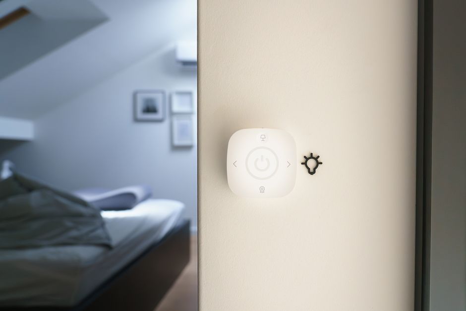 Imagem de um controle de iluminação inteligente na parede de um ambiente moderno, sugerindo automação residencial ou tecnologia doméstica.