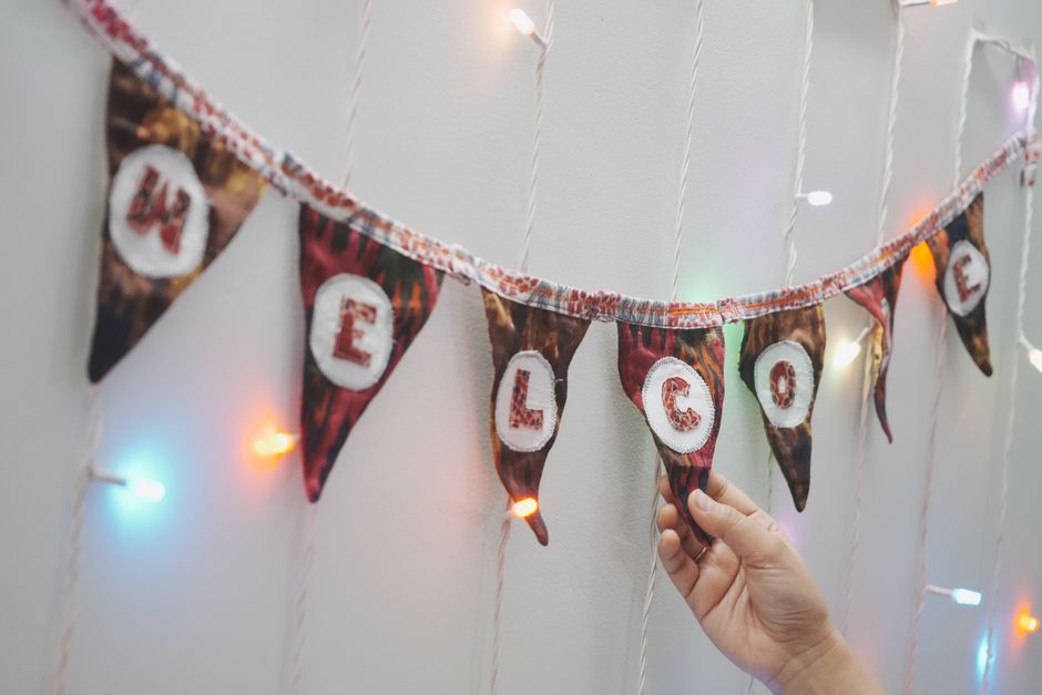 Pessoa decorando uma parede com uma faixa de festa e luzes coloridas, celebrando uma ocasião especial.