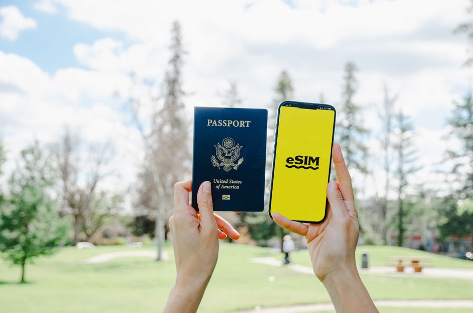 Pessoa segurando passaporte e celular com eSIM em um parque ao ar livre, simbolizando viagem internacional digital e conexão móvel.