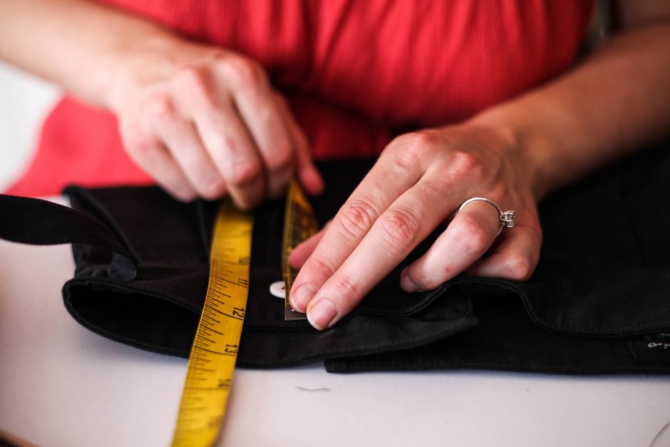 Pessoa ajustando roupas com uma fita métrica, simbolizando customização ou confecção de roupas.