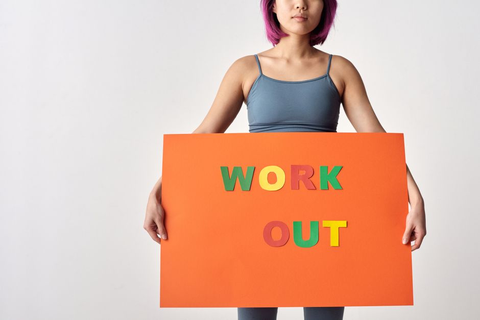 Jovem segurando cartaz com a frase ' WORK OUT ', simbolizando motivação para atividades físicas ou bem-estar.