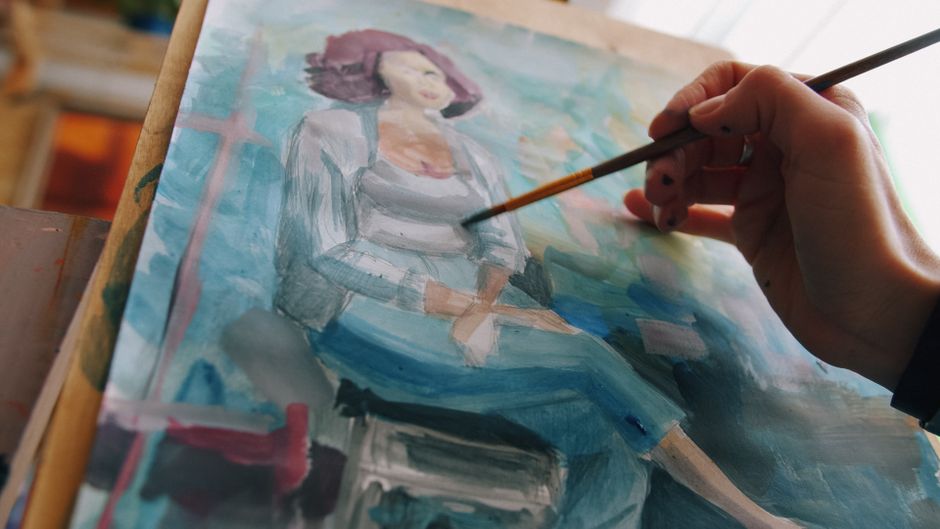 Artista pintando um retrato de uma mulher em uma tela, em um ambiente de estúdio artístico.