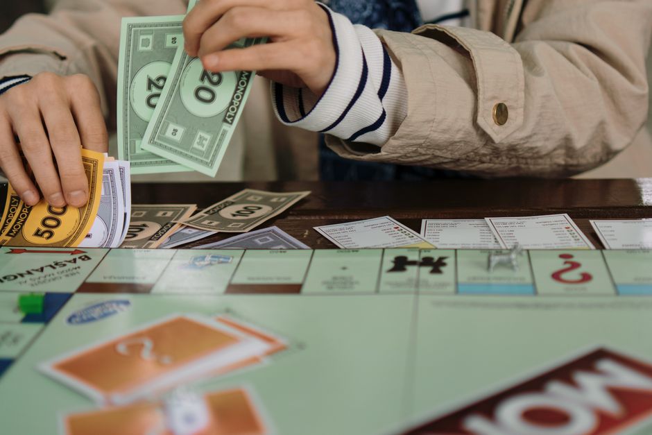 Pessoa jogando dinheiro e cartas de tabuleiro, ilustrando temas de jogos de azar ou estratégias financeiras.
