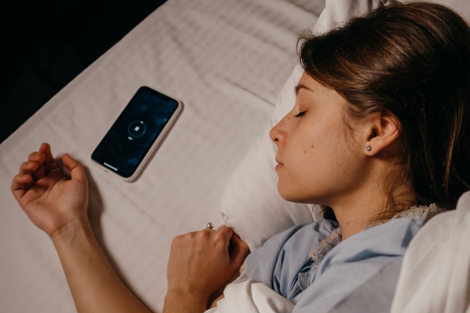 Mulher descansando na cama enquanto ouve música pelo celular, transmitindo sensação de relaxamento e descanso.