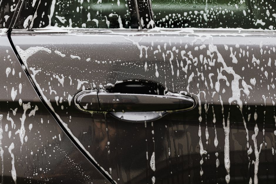 Imagem de uma porta de carro com manchas de sabão e água, como se estivesse sendo lavada, destacando a limpeza de veículos.