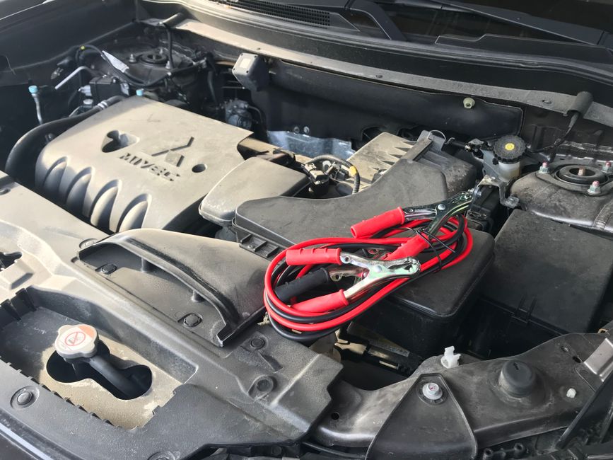 Imagem mostrando o motor de um carro com um kit de inicialização portátil e cabos de bateria, indicando manutenção ou emergência automotiva.