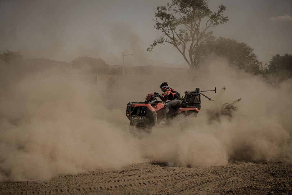 Pessoa pilotando uma motocicleta em uma trilha de terra com poeira levantada ao redor, em um cenário ao ar livre.