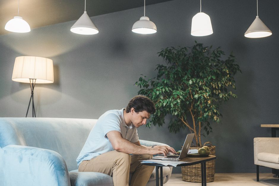 Homem trabalhando de forma concentrada em um ambiente doméstico ou de trabalho, utilizando um laptop com iluminação moderna.