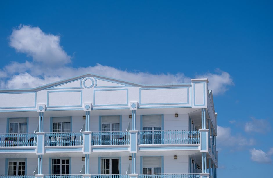 Imagem de um prédio residencial de cores claras sob um céu azul com nuvens, ideal para um blog sobre imóveis ou mercado imobiliário.