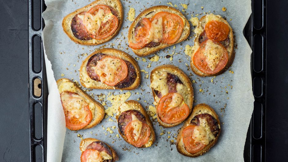 Mini torradas assadas com queijo, tomate e bacon, prontas para serem servidas como aperitivo ou lanche.
