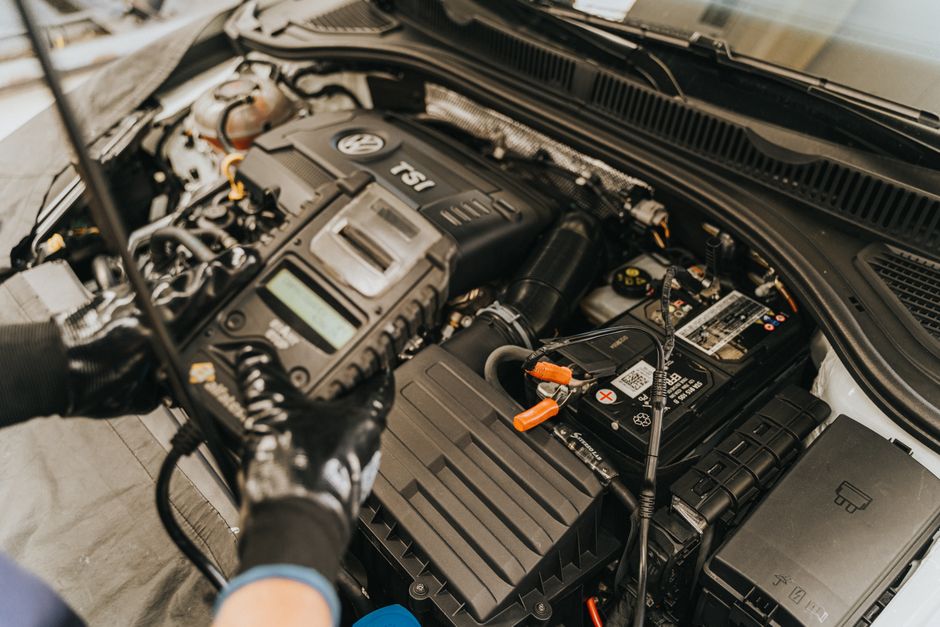 Imagem de um profissional realizando manutenção no motor de um carro, com foco em diagnóstico e inspeção de componentes automotivos.