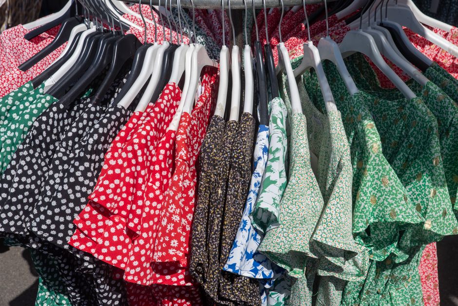 Imagem de blusas de diferentes cores e padrões expostas em cabides, agrupadas para venda em uma loja de roupas