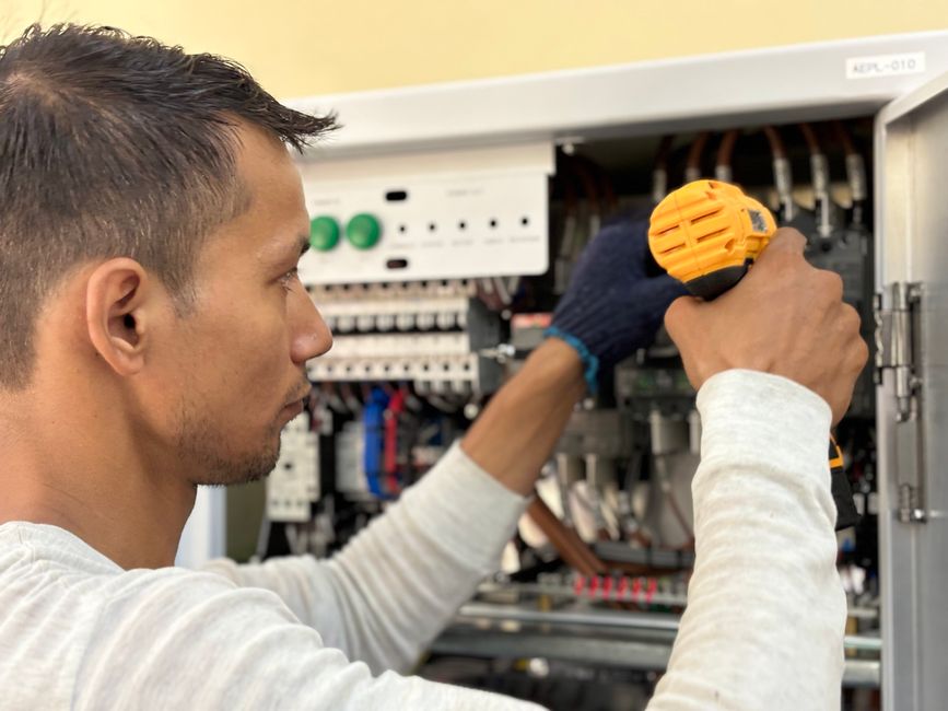 Técnico realizando manutenção elétrica em painel de controles industriais, destacando o trabalho técnico especializado.