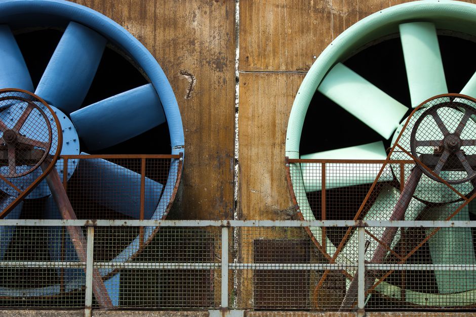 Imagem de duas grandes turbinas industriais instaladas em uma parede de ferro oxidado, com proteção de grade metálica na frente, simbolizando energia e tecnologia.