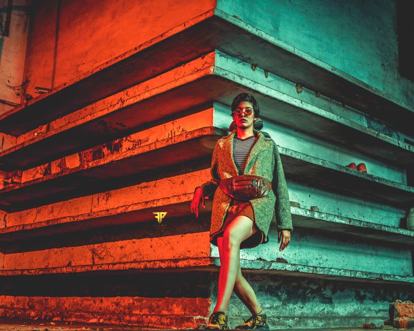 Mulher estilosa posando de forma confiante em ambiente urbano com iluminação colorida, destaque para moda e atitude ousada.