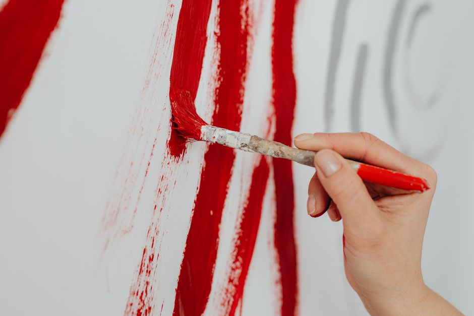 Pessoa pintando uma parede com destaque para a cor vermelha, simbolizando criatividade ou transformação.