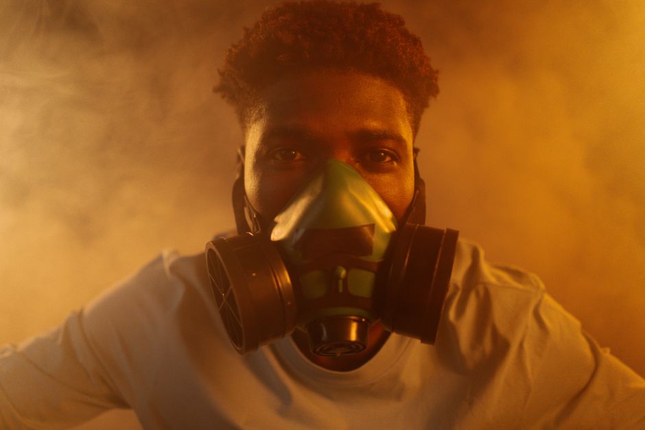 Homem usando máscara de proteção respiratória em ambiente com fumaça ou poluição, simbolizando conscientização sobre saúde e segurança no trabalho ou proteção ambiental.