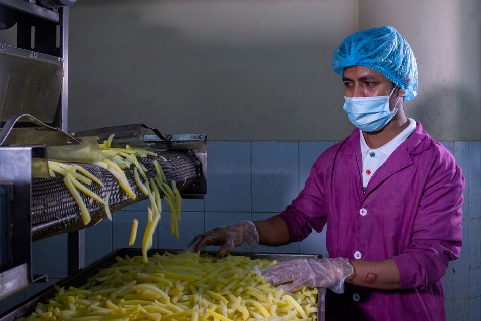 Pessoa operando máquina de fabricação de alimentos processados em ambiente de produção alimentícia industrial.
