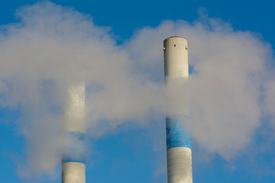 Chaminés industriais emitindo fumaça contra o céu, simbolizando poluição ou energia industrial.